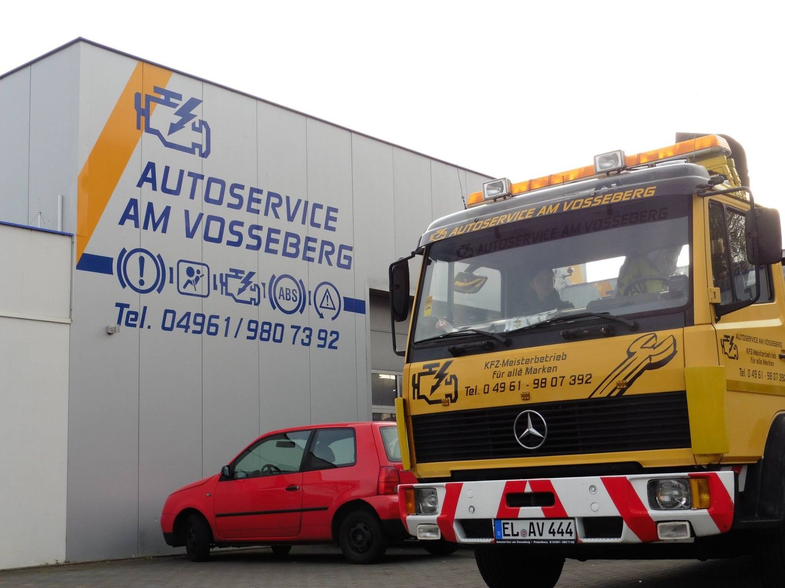 Älterer gelber Abschleppwagen vor dem Schild Autoservice am Vosseberg