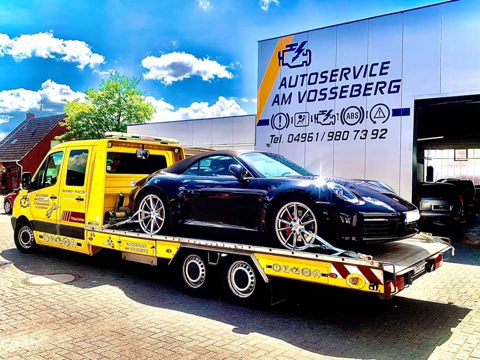 Gelber Plateauwagen mit Sportwagen vor dem Werkstattschild