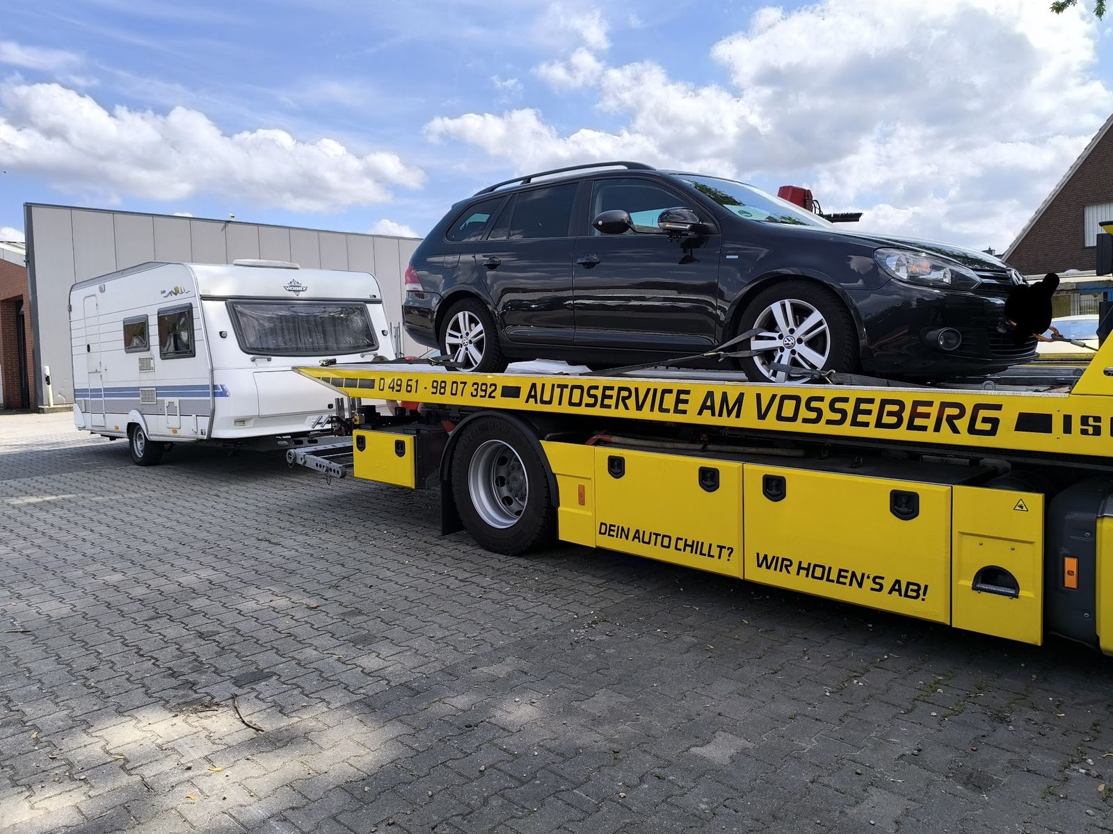 Gelber Abschleppwagen mit der Aufschrift Dein Auto chillt? Wir holen's ab! und einem Wohnwagen am Haken